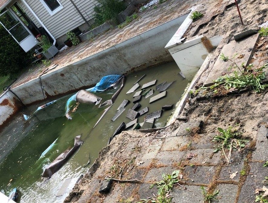 Debris floating in a narrow concrete canal beside a walkway and buildings.