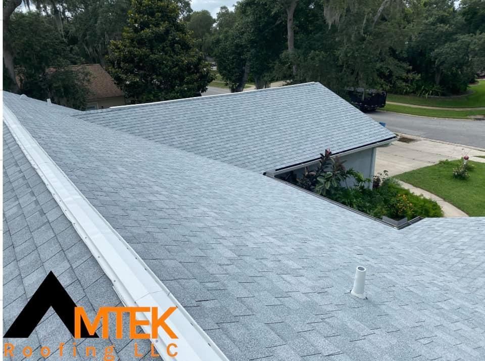Aerial view of a gray-shingled roof on a house with trees and a street nearby