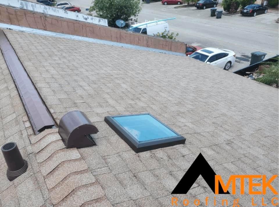 Roof with shingles, vent pipes, and a skylight overlooking a parking lot.
