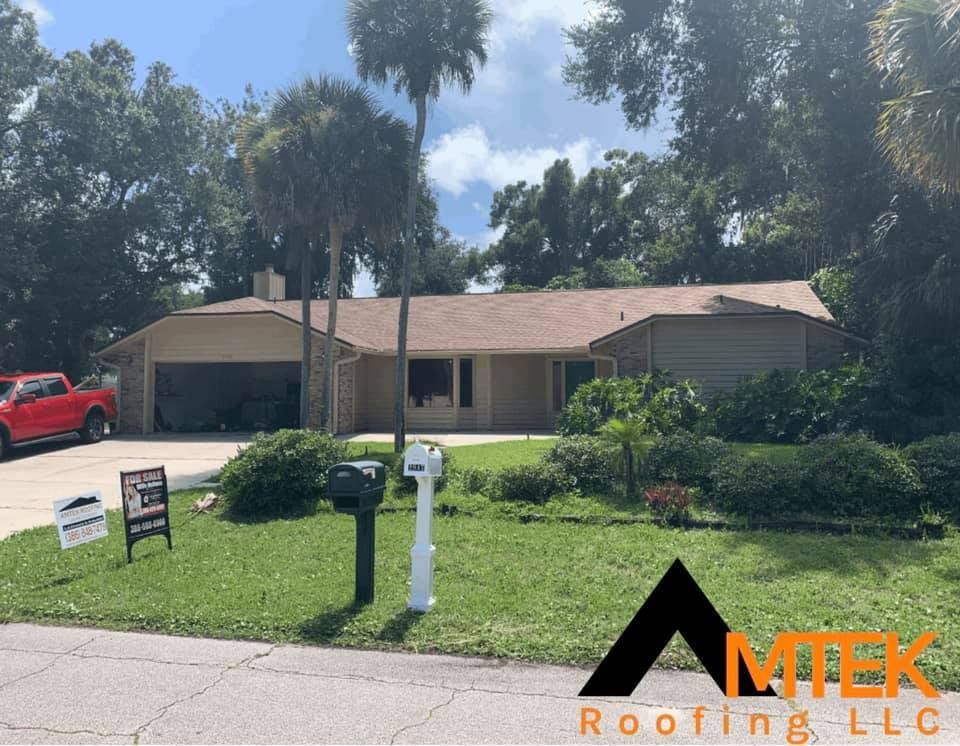 Single-story beige house with tan roof, front lawn, trees, and a roofing company logo watermark.