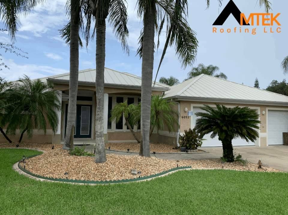 Single-story beige home with a tiled roof, palm trees, and a green lawn under a cloudy sky.