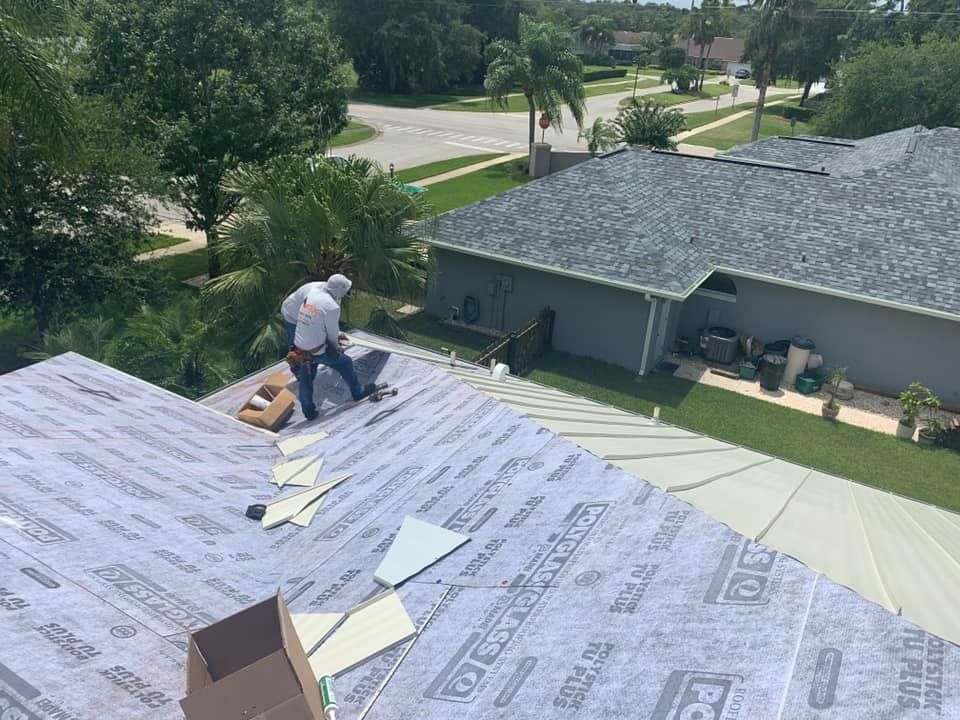 Workers installing roofing shingles on a house roof beside a suburban street