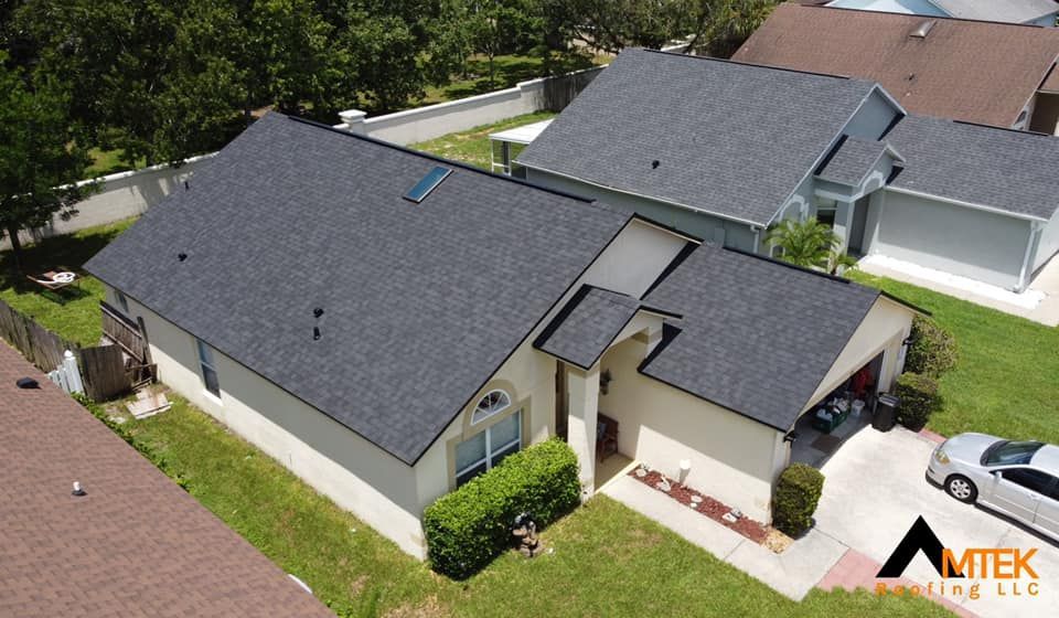 Aerial view of two gray-roofed suburban houses with driveways, lawns, and a parked white car.