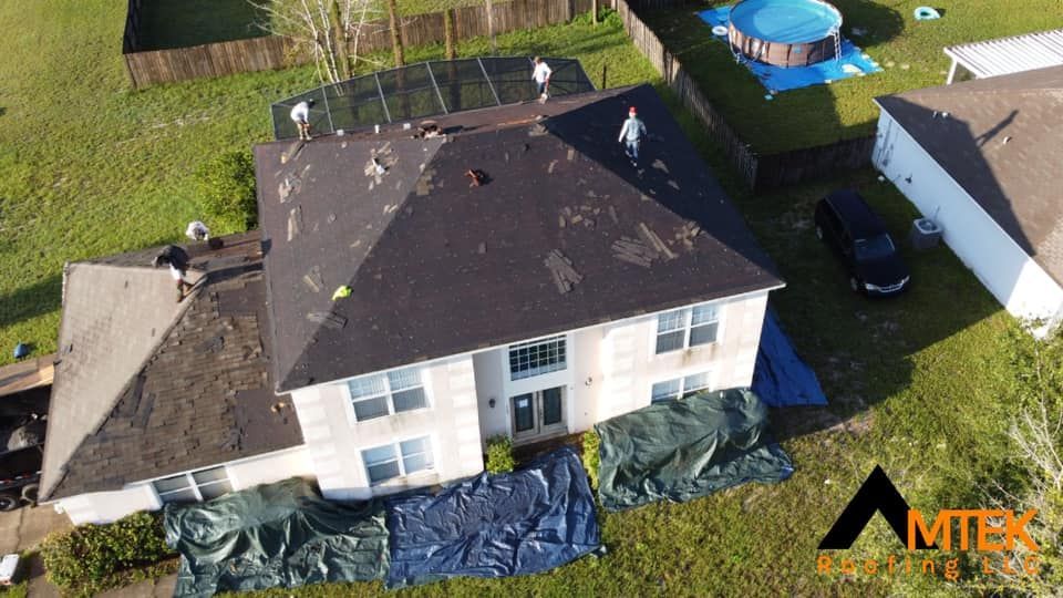 Aerial view of a house with a dark roof and solar panels, surrounded by a yard with construction tarps.