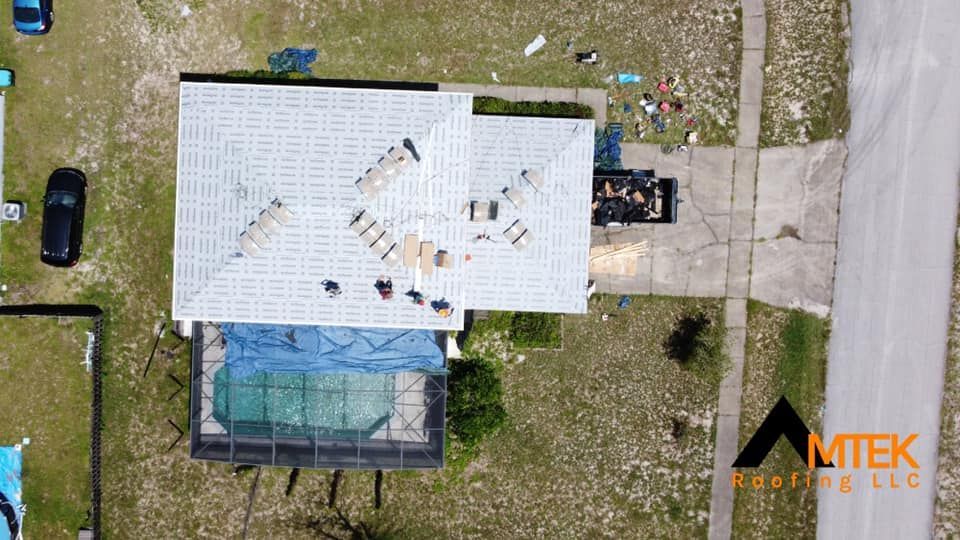 Aerial view of a white-roofed house with rooftop workers and a fenced backyard pool.