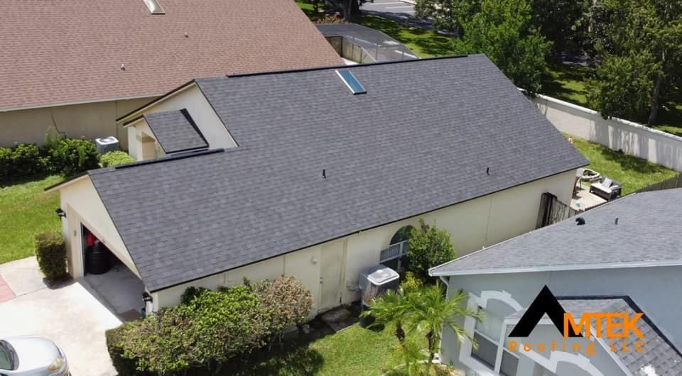 Aerial view of a gray-roofed house with a white garage, driveway, and green yard.