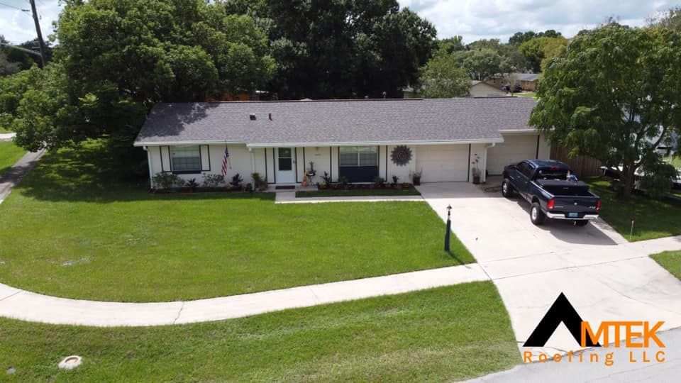 Single-story white house with gray roof, green lawn, and black truck in the driveway under trees.