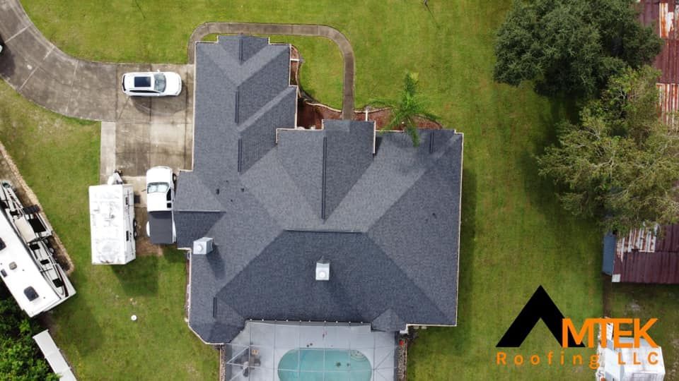 Aerial view of a house with a gray roof, driveway, lawn, and a pool in the backyard.