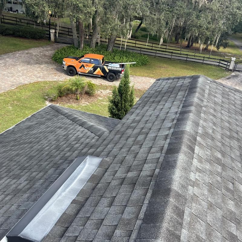 Worker measuring a shingled roof ridge with a yellow tape measure.