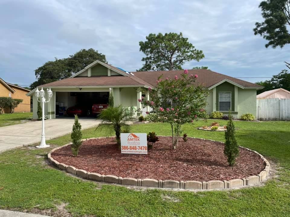 Single-story house with a red roof, front lawn, and landscaped circular flower bed with a sign.