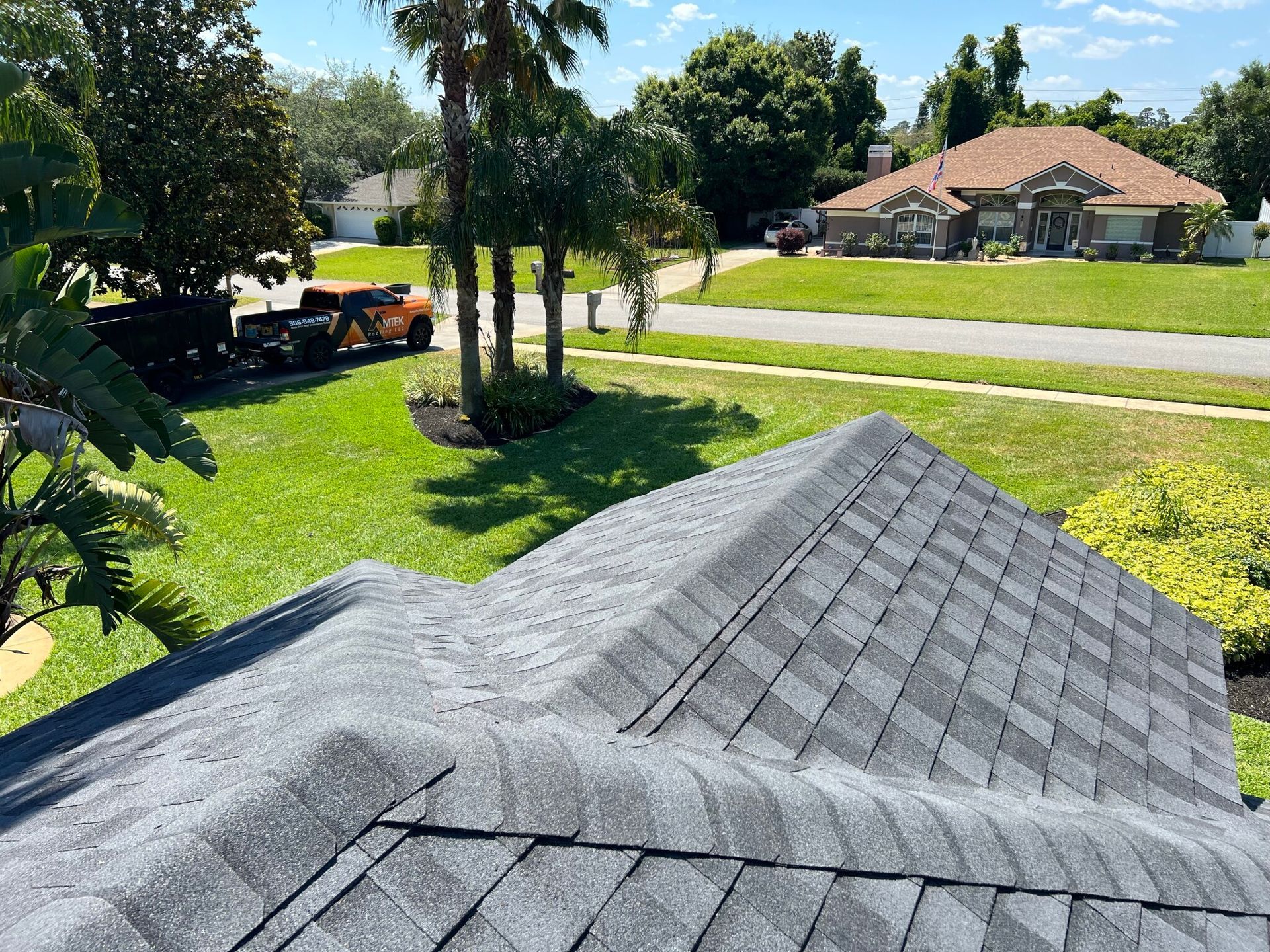 View from a roof over a sunny suburban street with lawns, trees, and a house across the road
