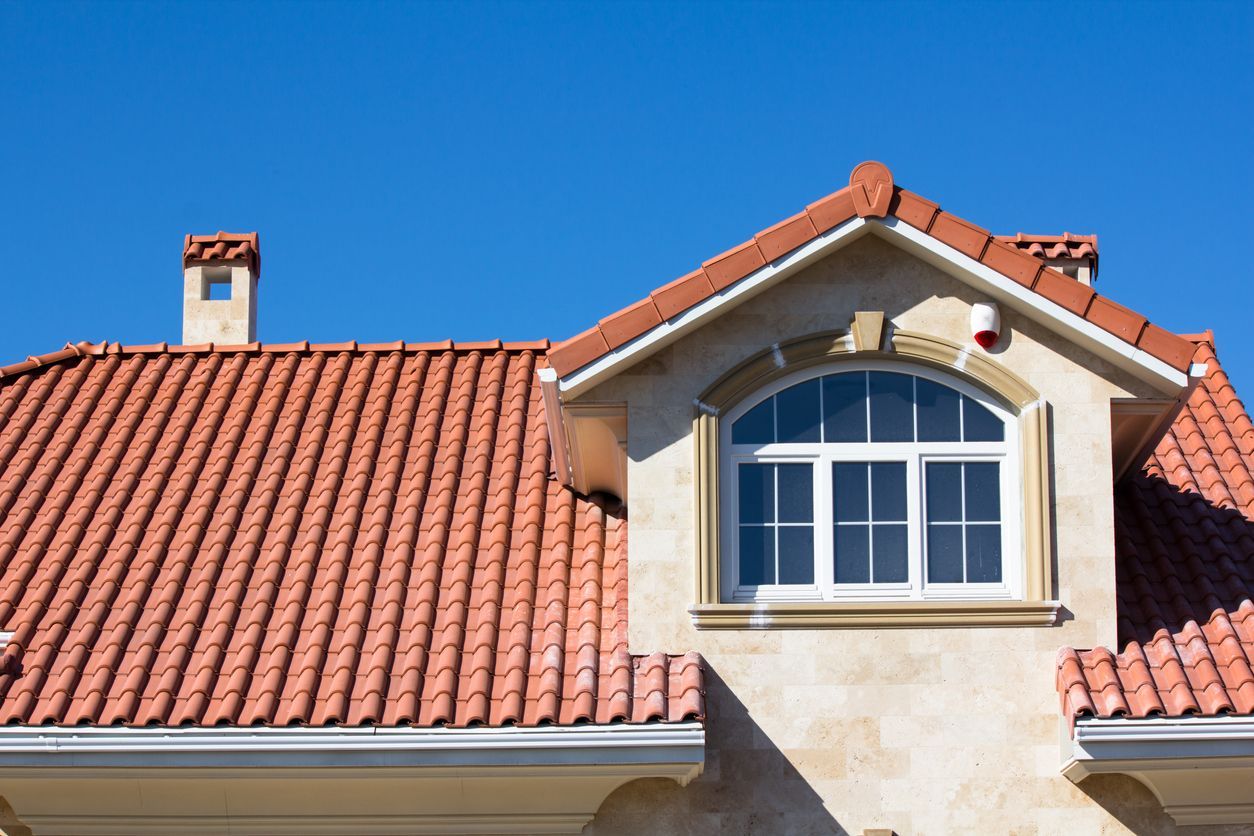 Red-tiled house roof with a dormer window and beige exterior under a clear blue sky