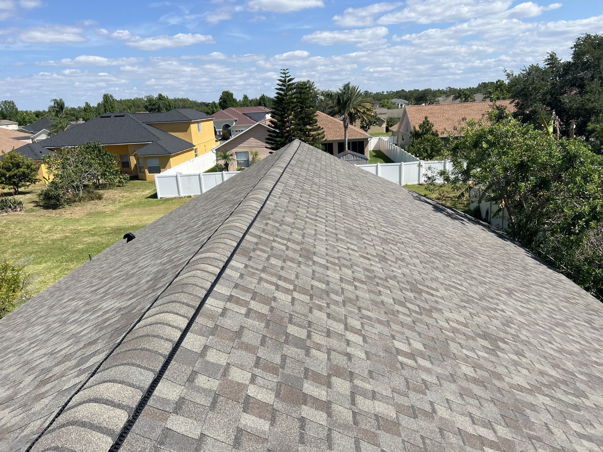 Rooftop view over suburban houses and trees under a partly cloudy sky.
