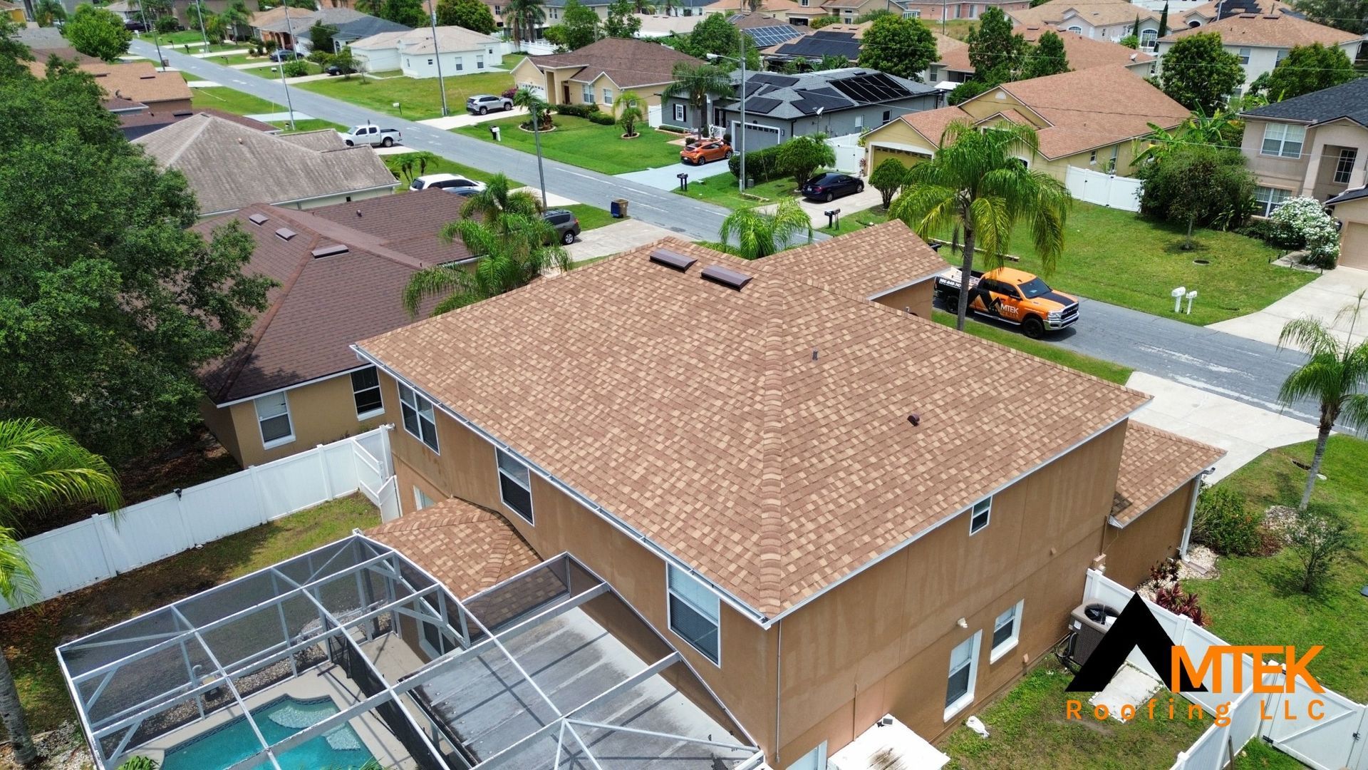 Aerial view of a suburban house with a tan roof, backyard pool cage, and tree-lined neighborhood streets.