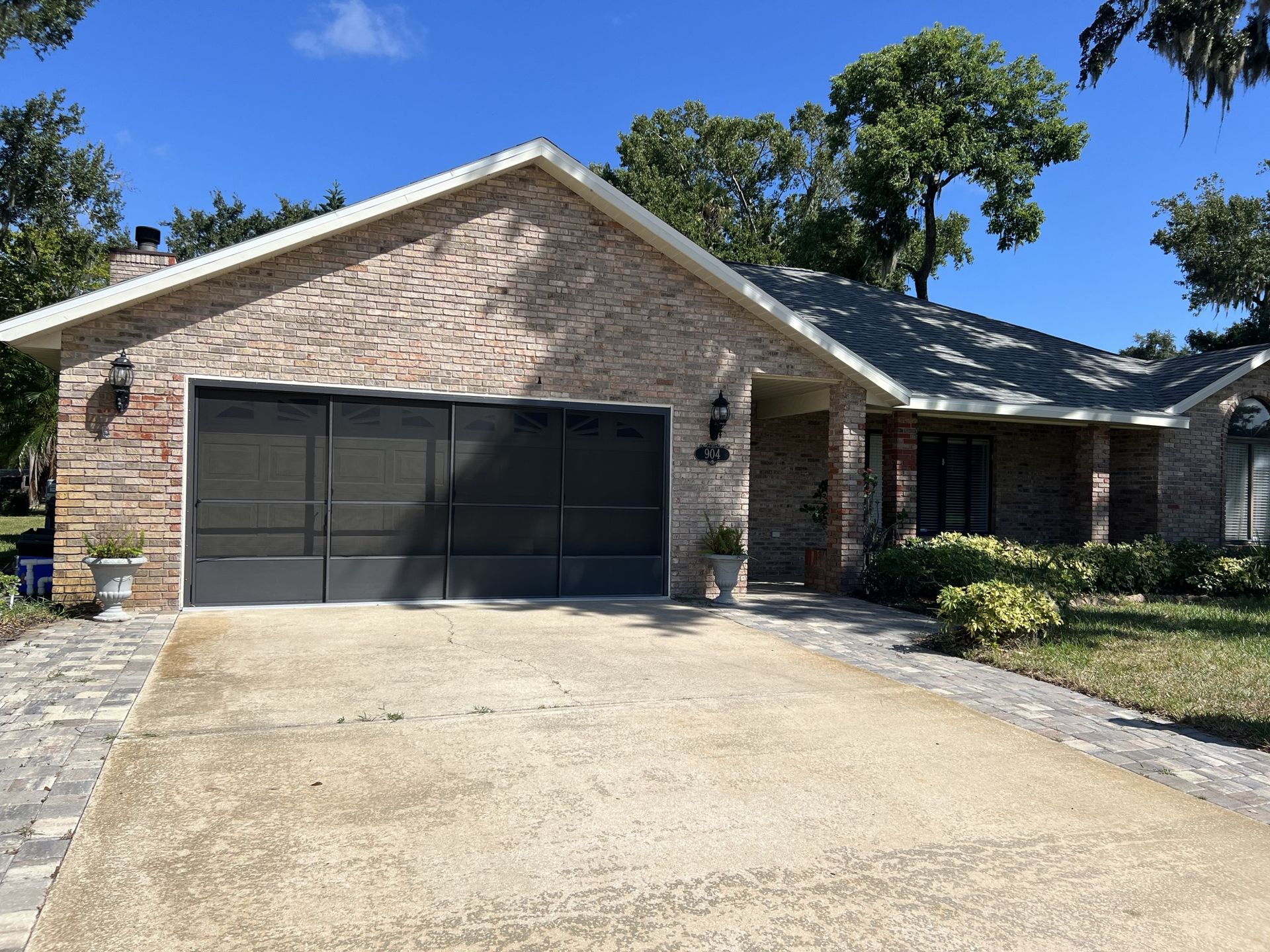 Brick suburban house with black garage door and a wide concrete driveway under a clear blue sky