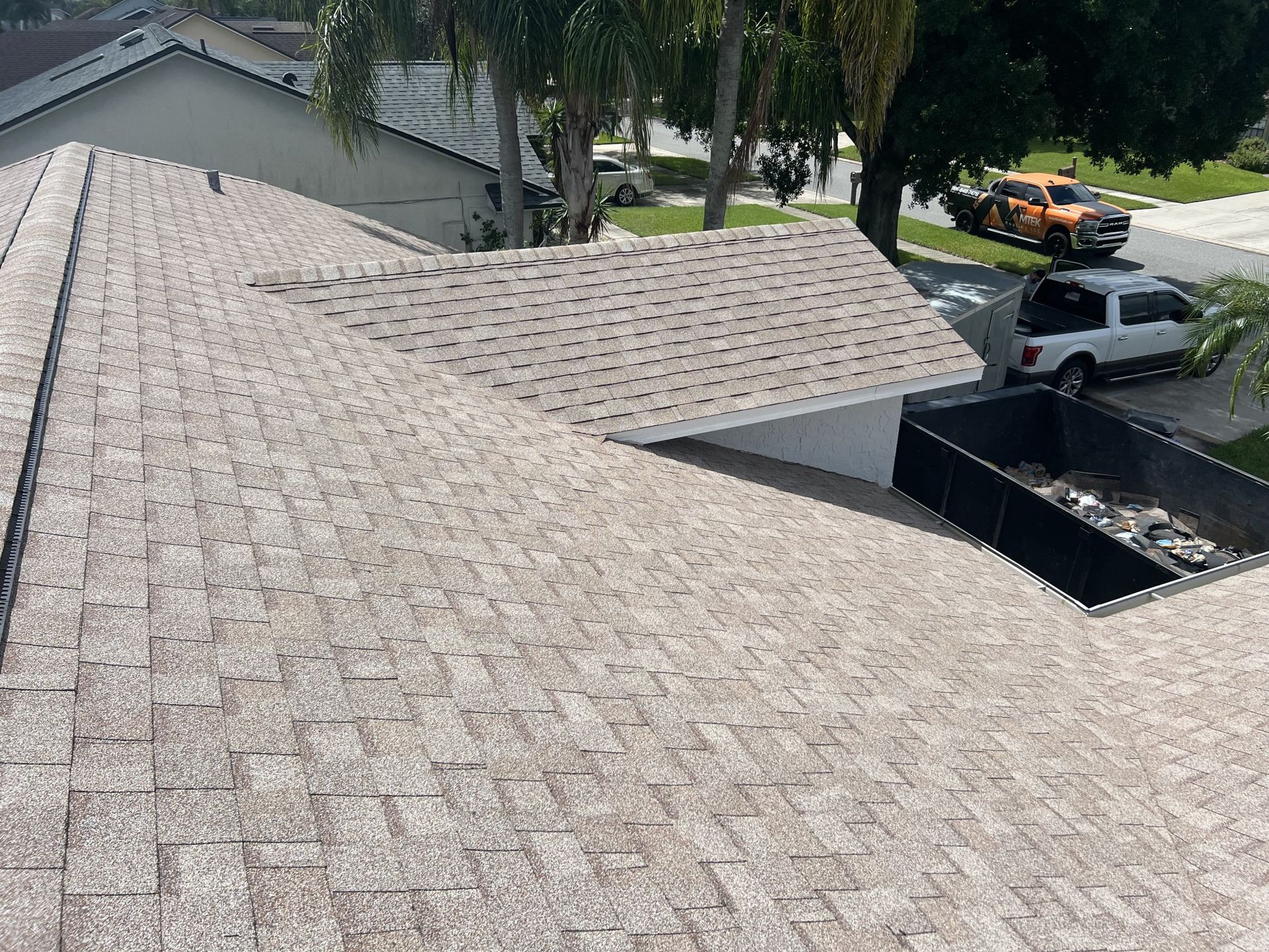 Roof shingles and a covered patio over a residential backyard, with parked vehicles visible below.