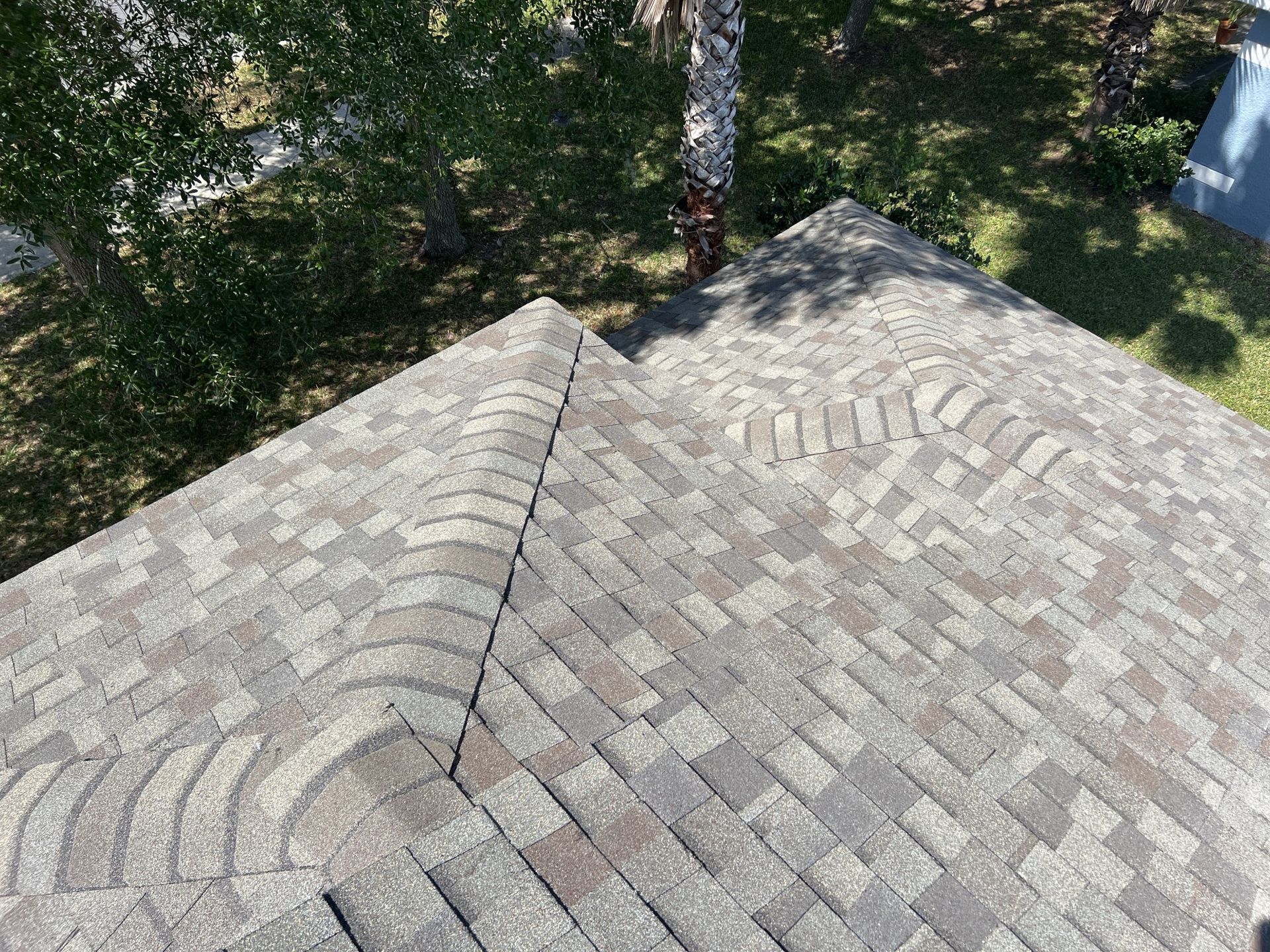 Gray shingle roof peaks beside a tree and grassy yard, viewed from above