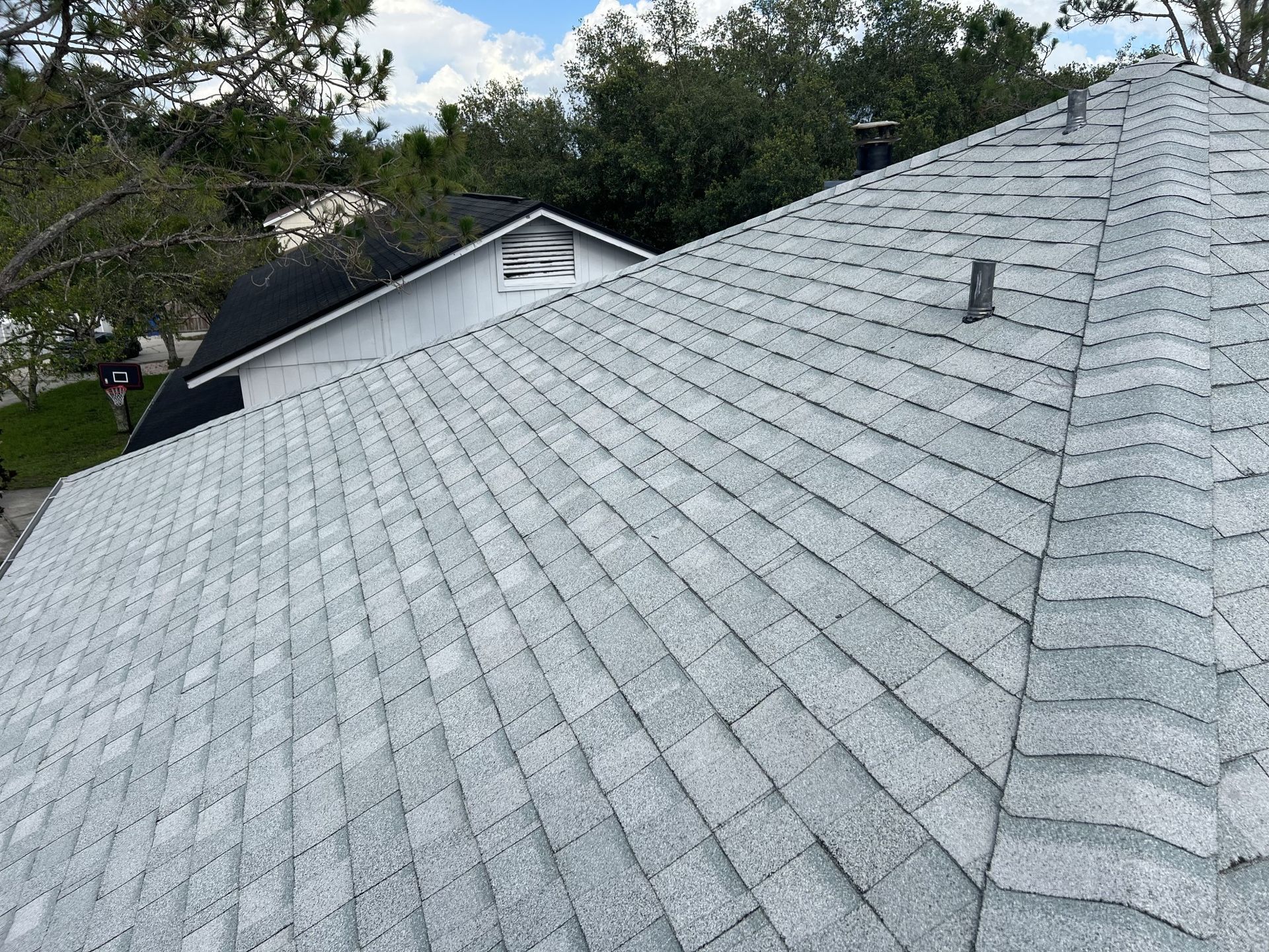 Gray shingled roof with a satellite dish and trees in the background