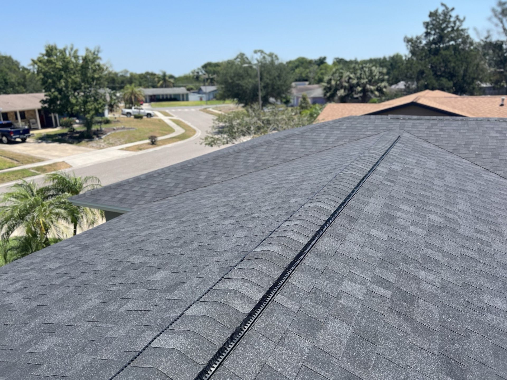 View from a roof over a suburban neighborhood, with dark gray shingles and a curved street below.
