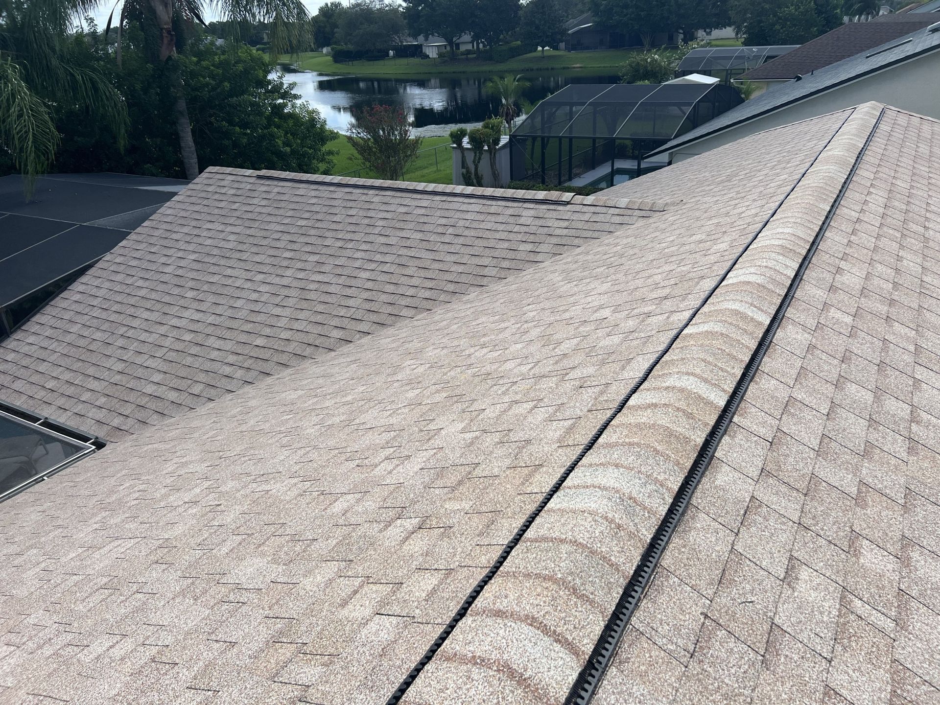 View from a shingled rooftop overlooking trees, neighboring roofs, and water in the distance