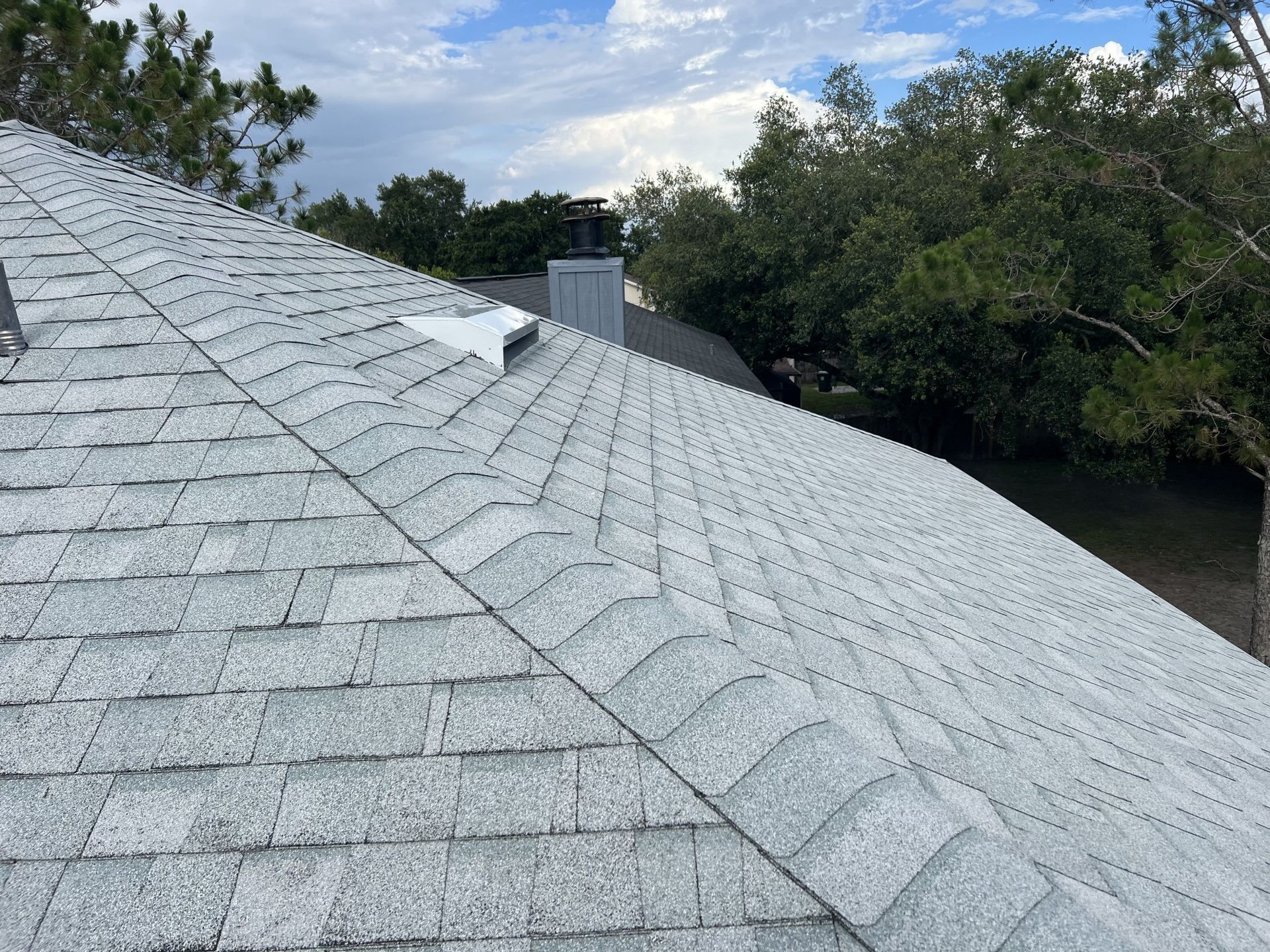 Rooftop with a white metal roof and a silver ventilation turbine in the foreground.