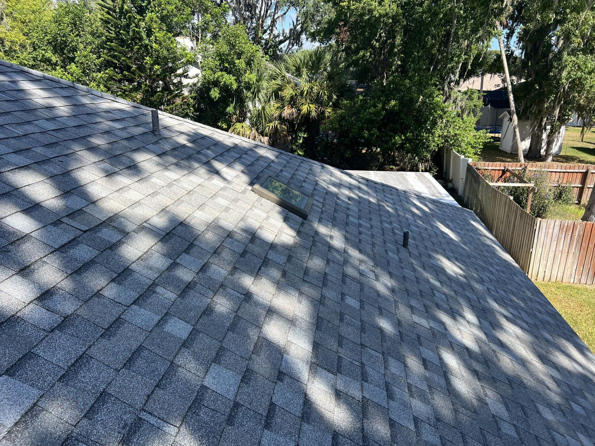 Roofing worker installing gray shingles on a steep roof slope