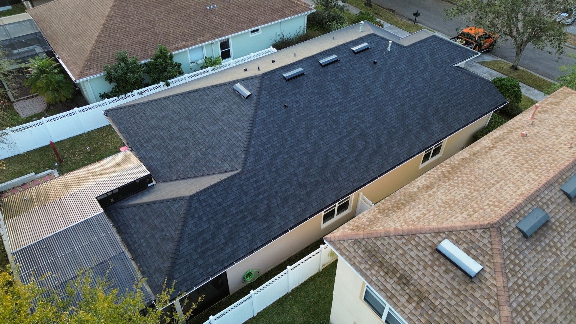 Aerial view of a house with a dark shingled roof and nearby neighboring rooftops.
