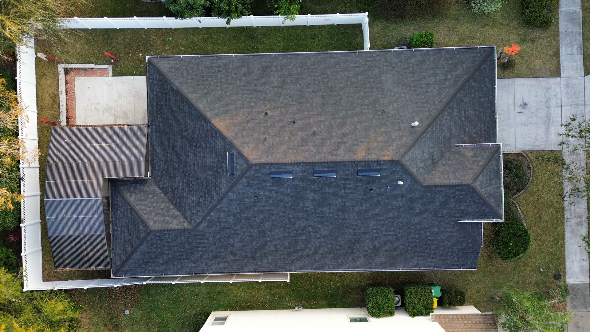 Aerial view of a dark gray shingled house roof with surrounding yard and driveway.