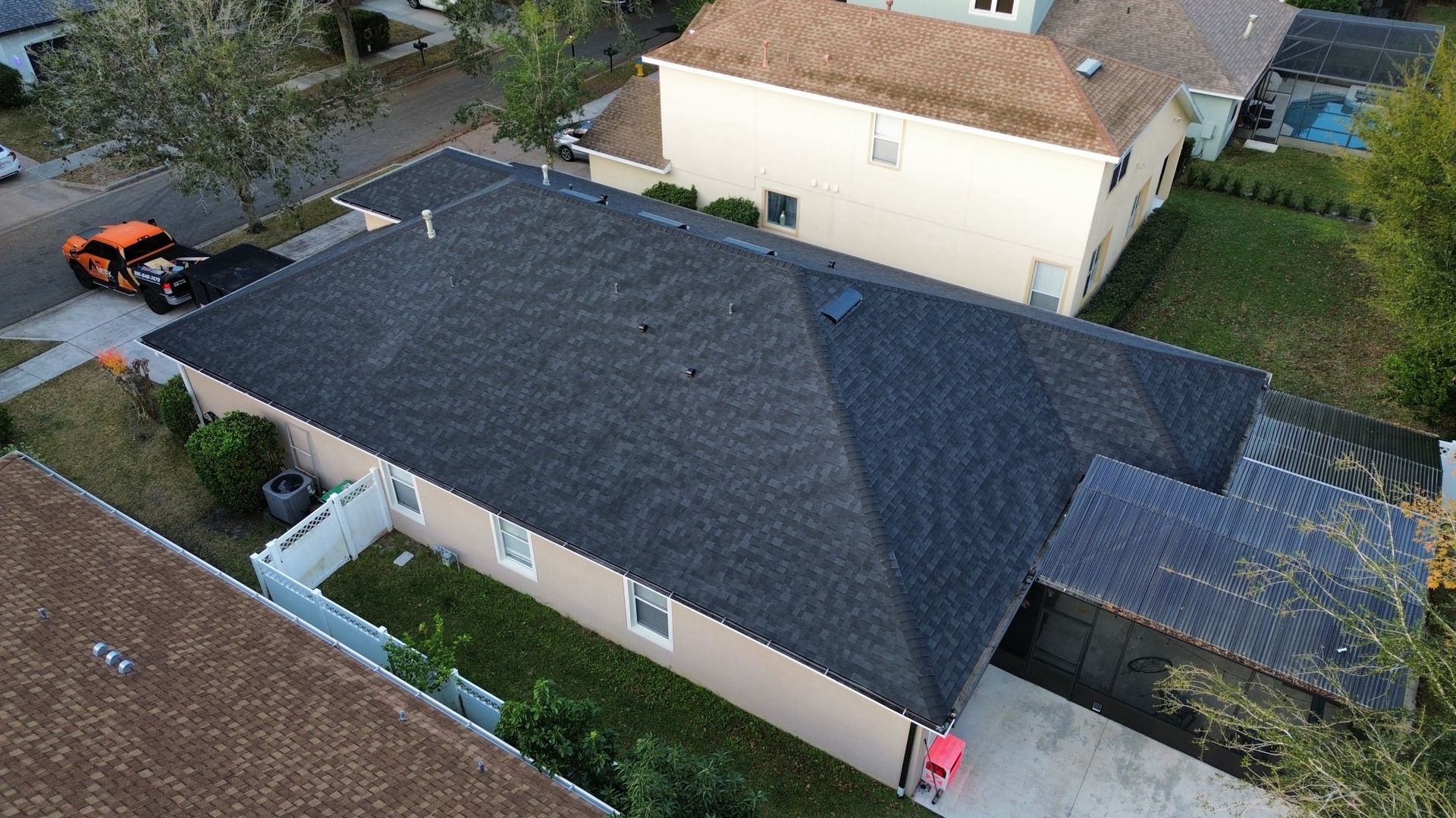 Aerial view of a dark gray roofed house with a driveway, yard, and neighboring homes.