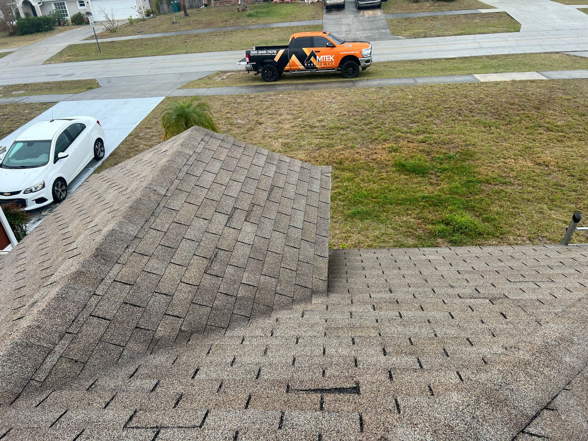 Rooftop view of a suburban street with a white car, orange truck, and grassy yard below.