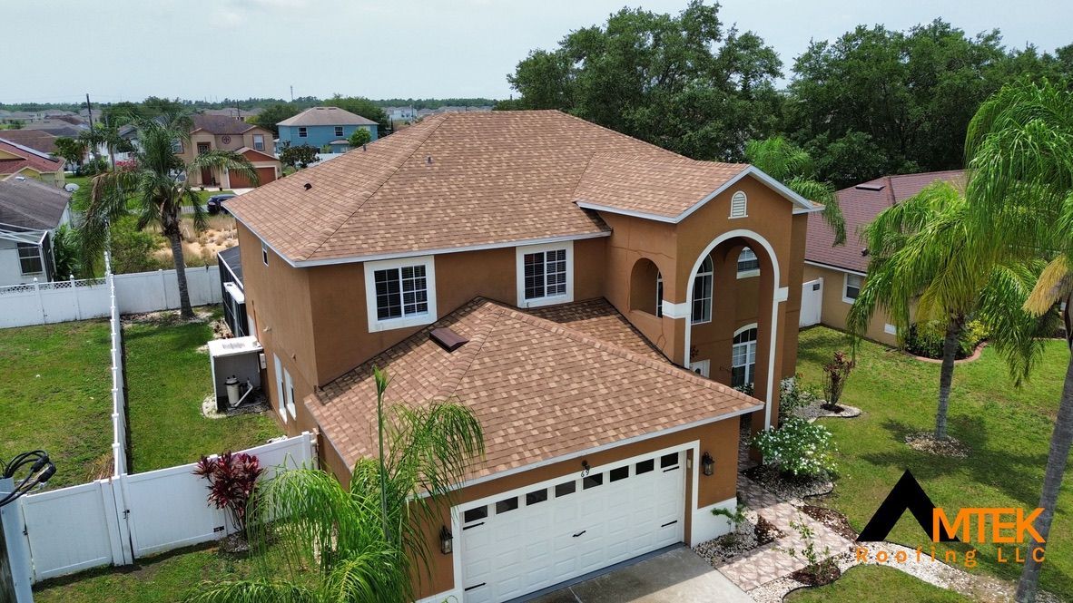Aerial view of a two-story tan house with a tiled roof, white garage, and green yard in a suburban neighborhood
