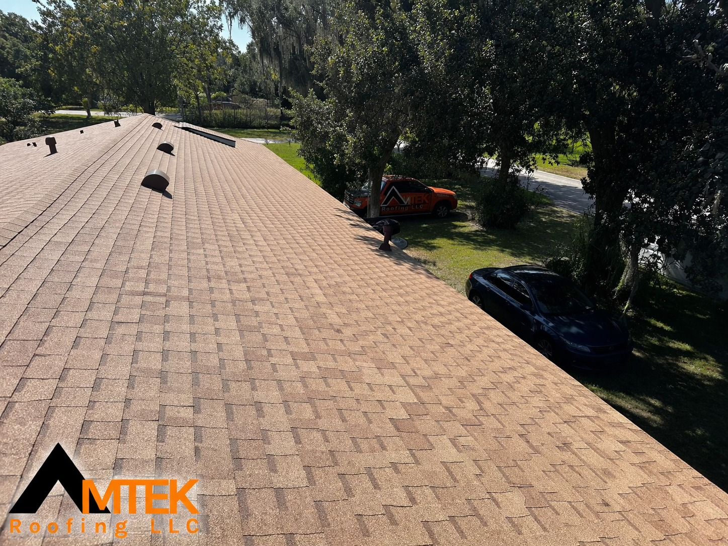 Roof with tan shingles, several vents, and trees shading a yard below.