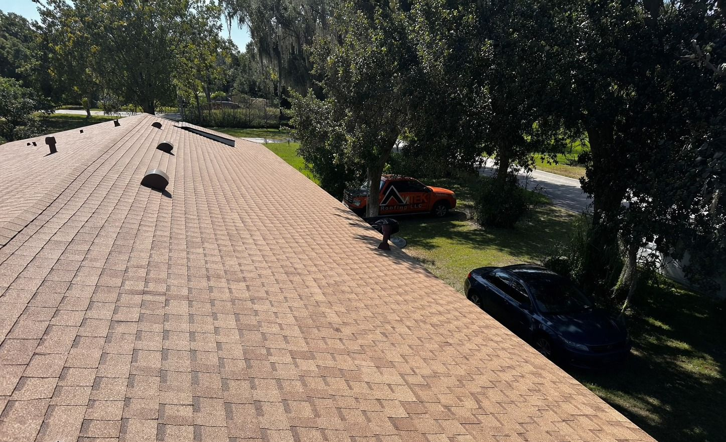 Rooftop with solar panels under trees beside a driveway and parked vehicles