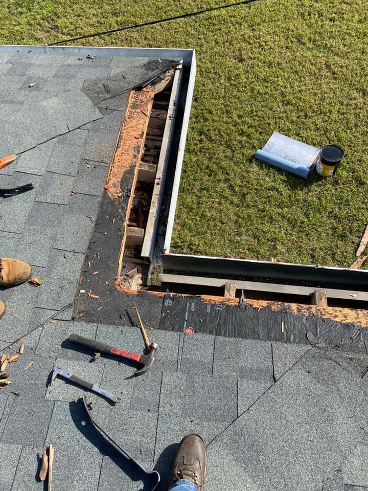Roof repair in progress on a shingled roof beside a grassy yard, with tools and exposed roofing