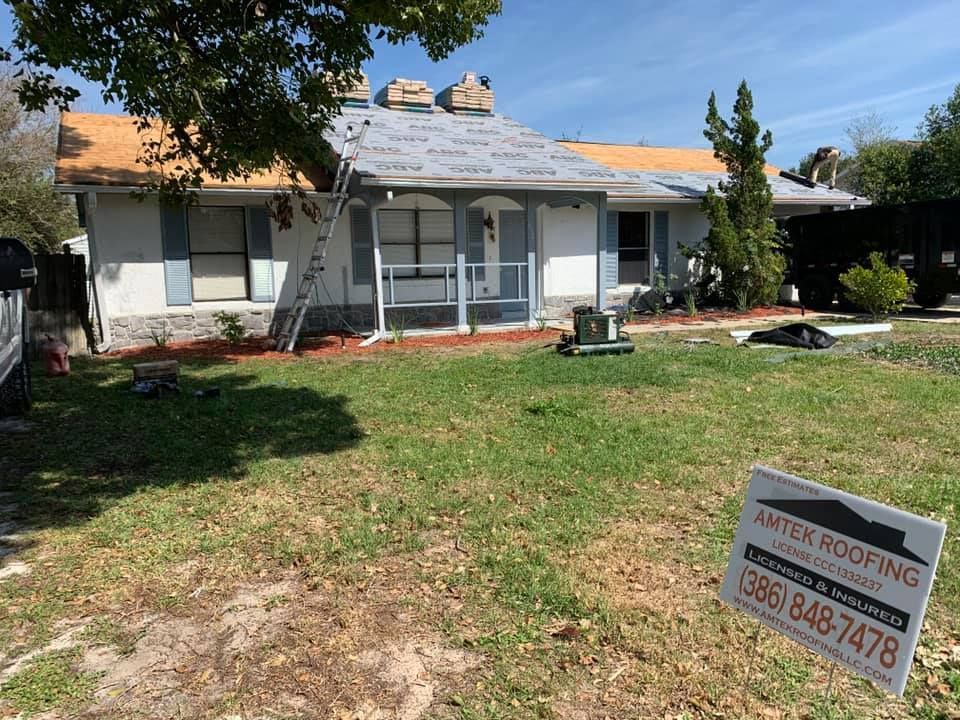 House with roof repairs and ladder in front yard, roofers’ sign in lawn