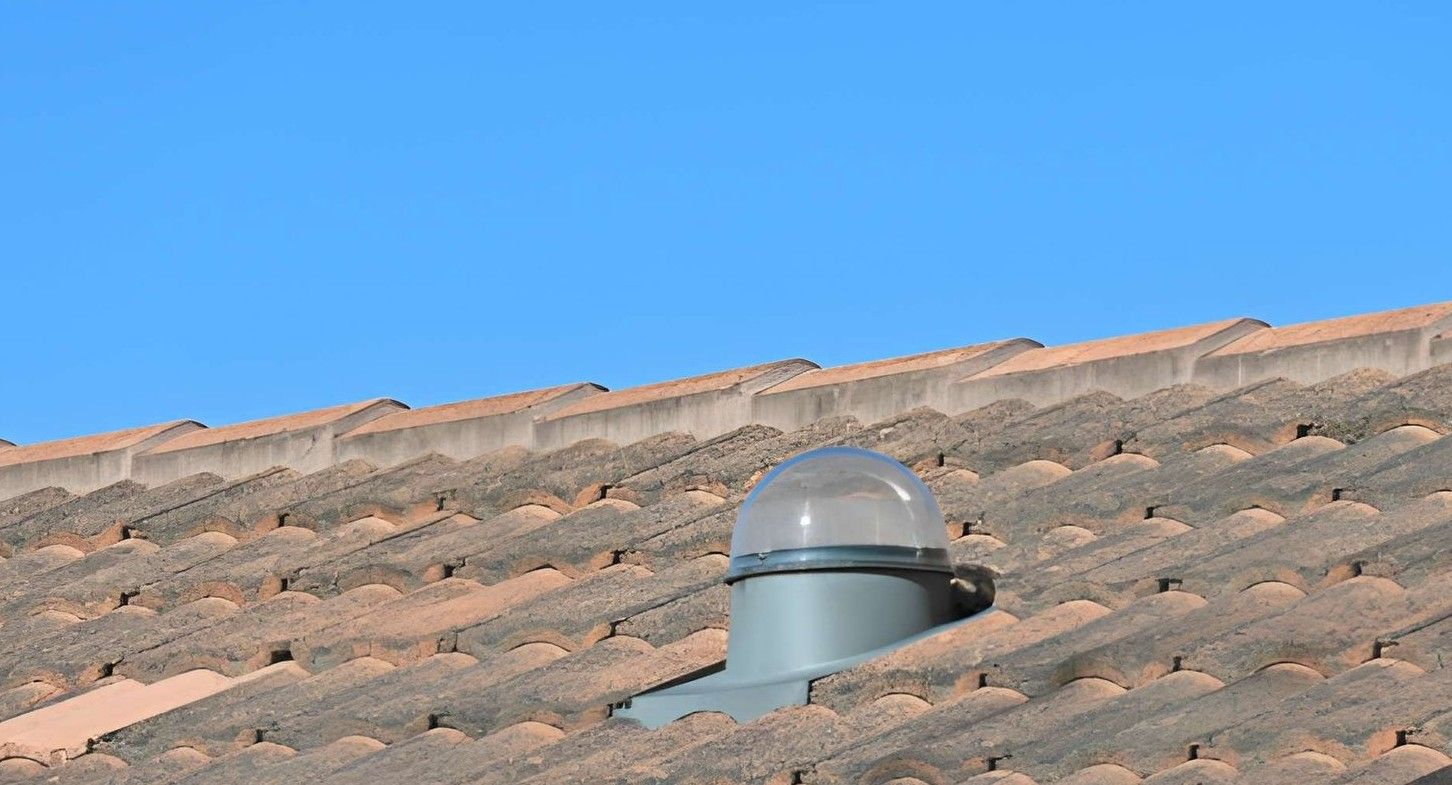Flat rooftop with a central vent and autumn trees under bright sunlight