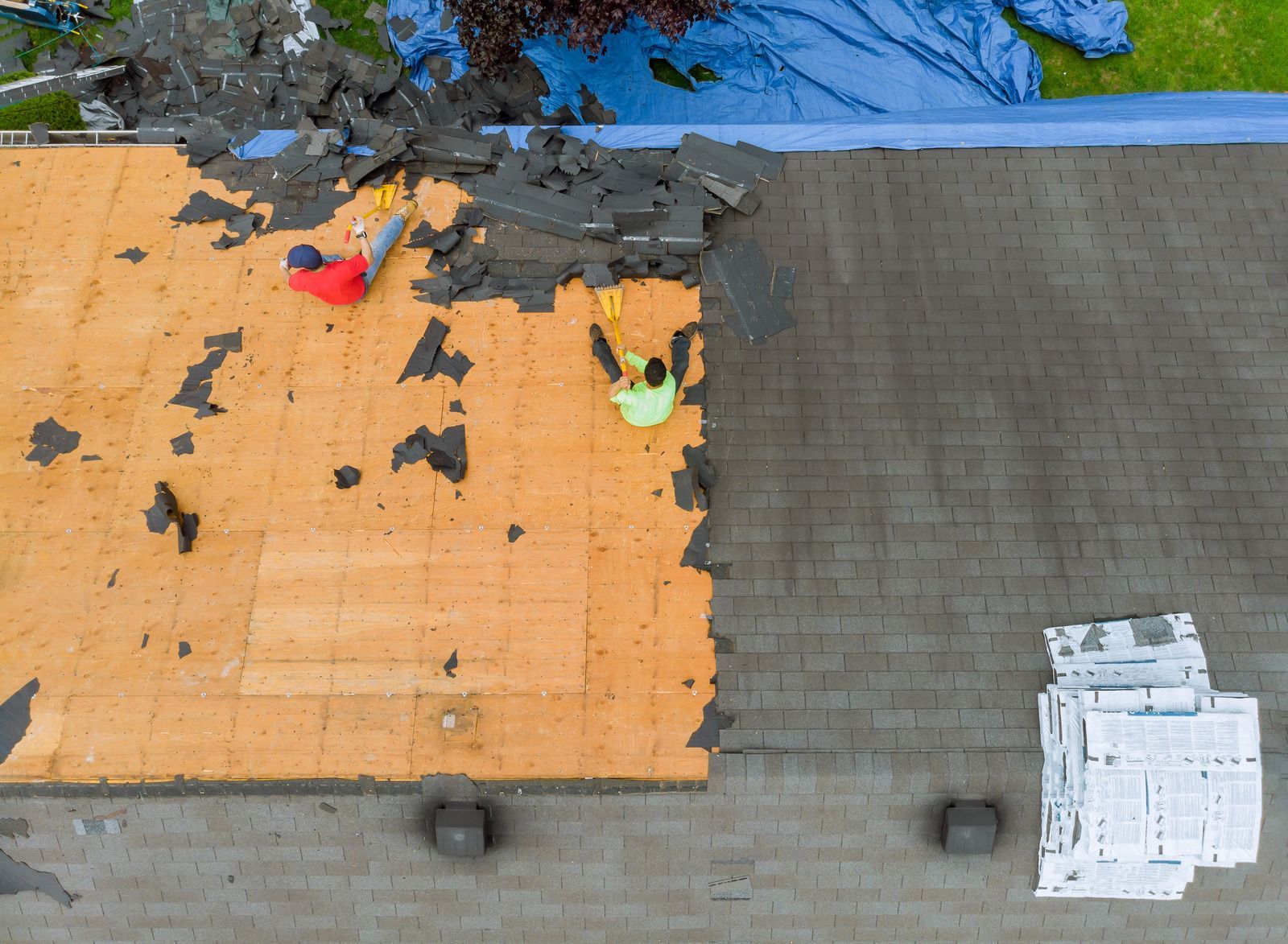 Worker in blue helmet and harness on a steep shingled roof, using a rope for safety.