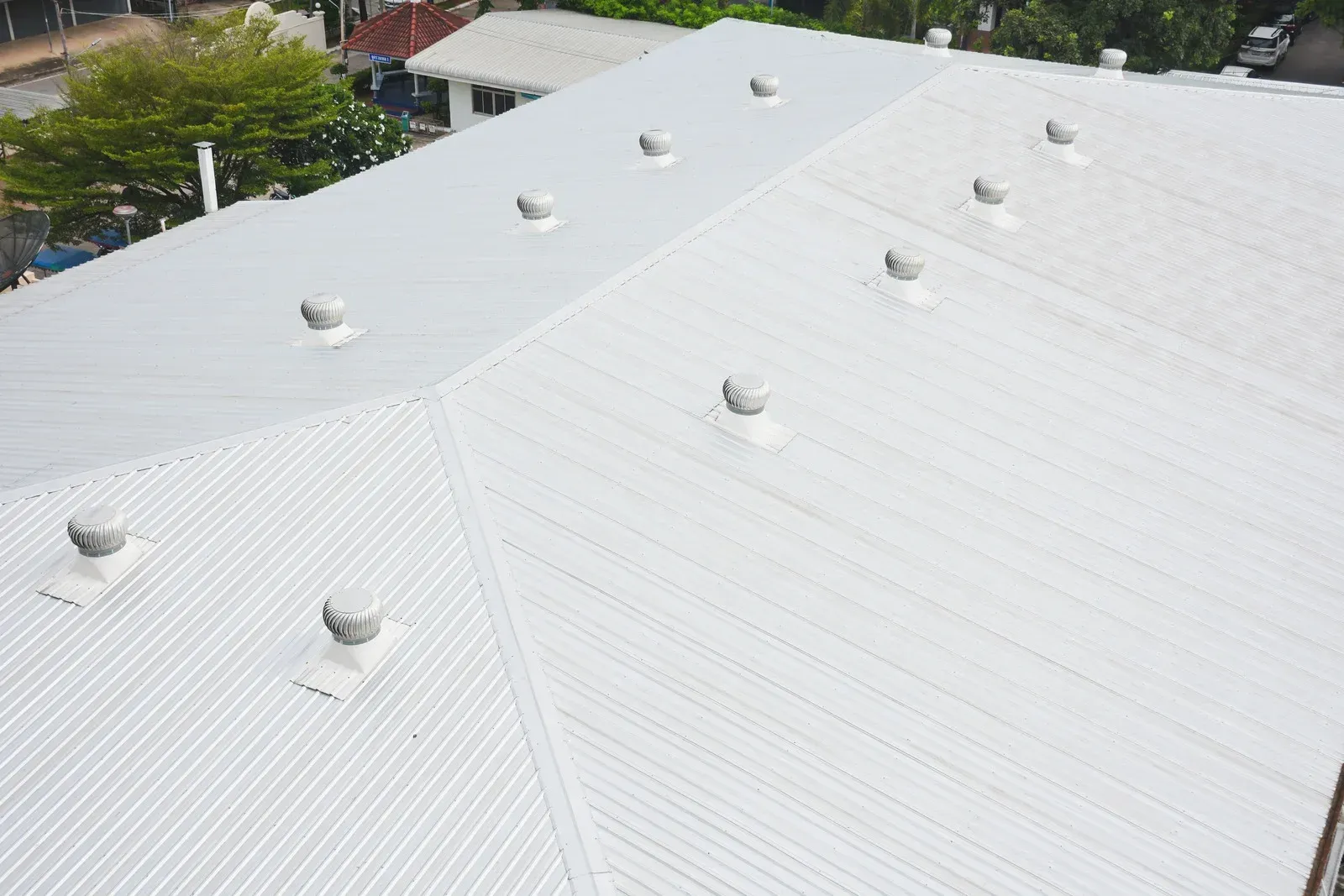 Rooftops of clustered buildings with gray-green metal roofs and multiple white chimneys.