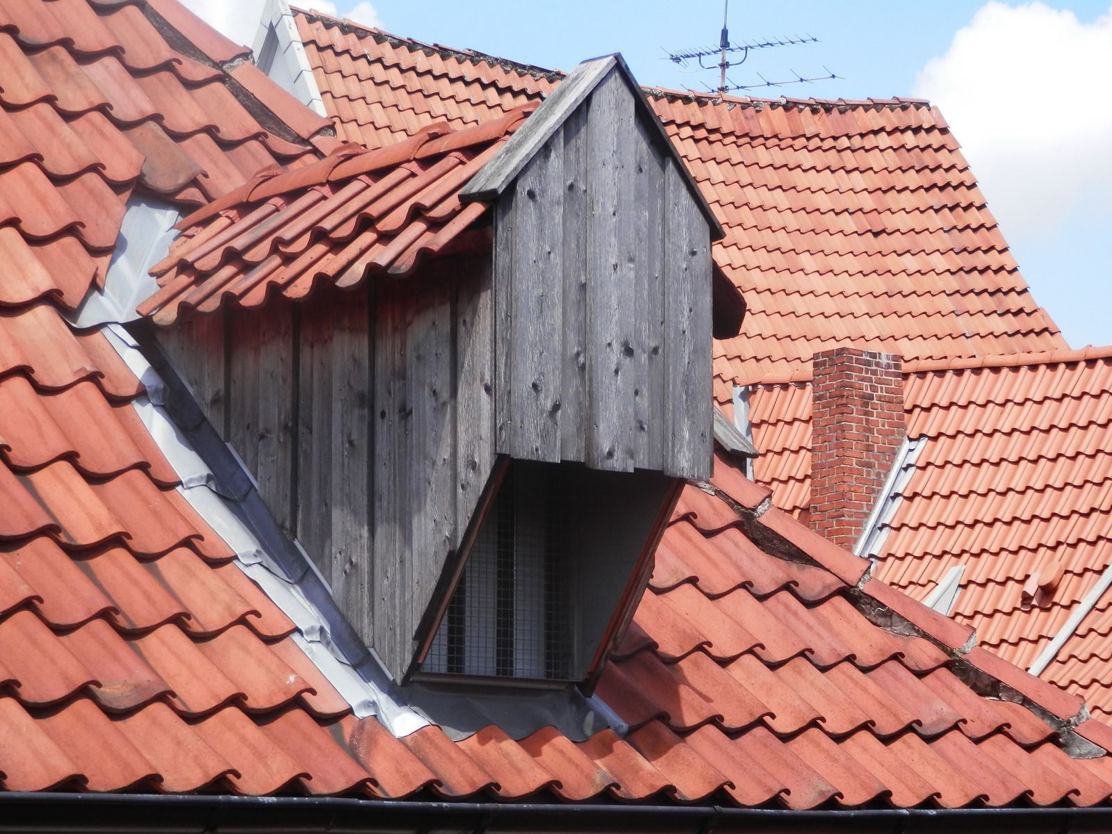 Red clay tile rooftops with a weathered wooden dormer and small window.