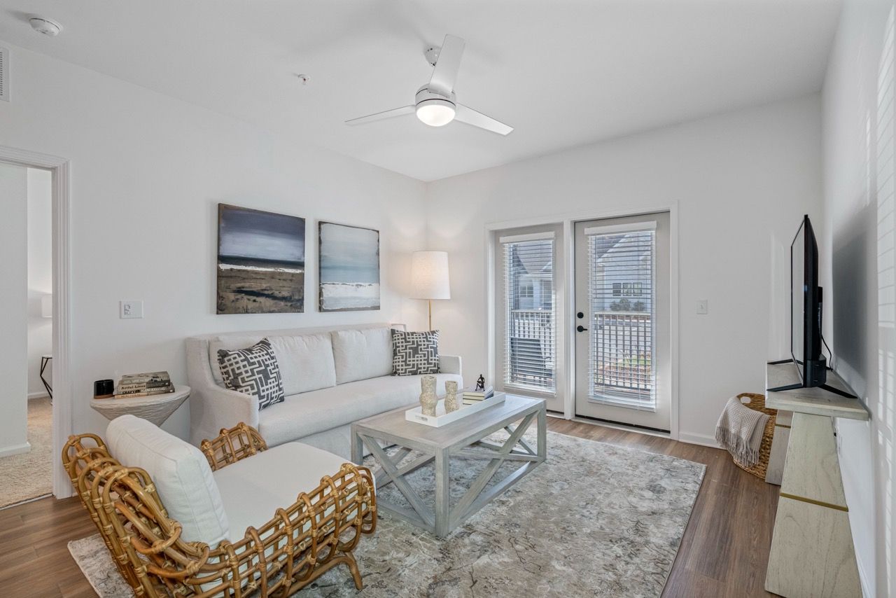Living room with white sofa, wicker chair, coffee table, TV on a stand, and French doors.