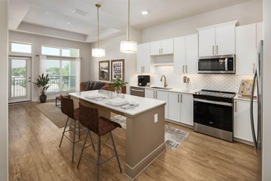 A kitchen with white cabinets and stainless steel appliances and a large island in the middle.
