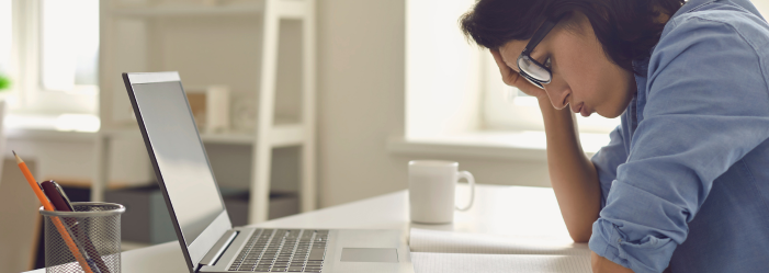 Una mujer está sentada en un escritorio con la cabeza entre las manos frente a una computadora portátil.