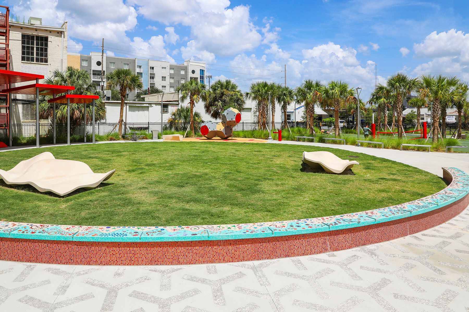 A circle of grass with a brick border in a park with palm trees in the background.