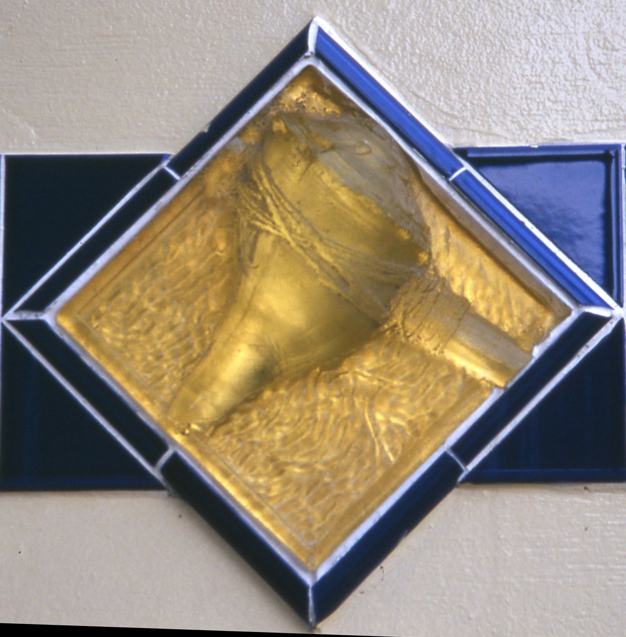 A diamond shaped tile with a gold object in it