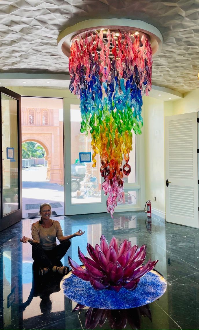 A woman is sitting in a lotus position in front of a rainbow chandelier.