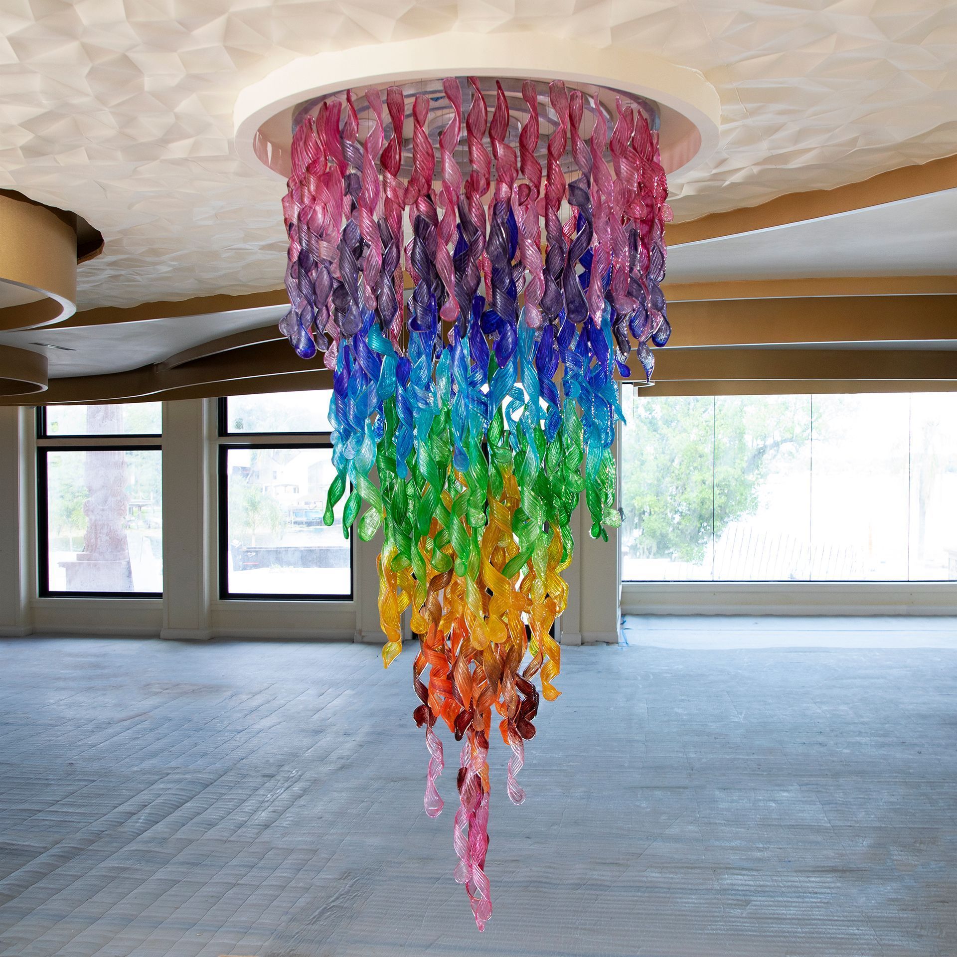 A rainbow colored chandelier hangs from the ceiling in an empty room