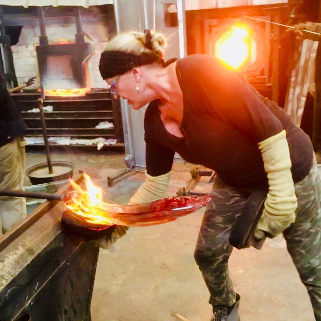 A woman is working on a piece of glass in front of a fire