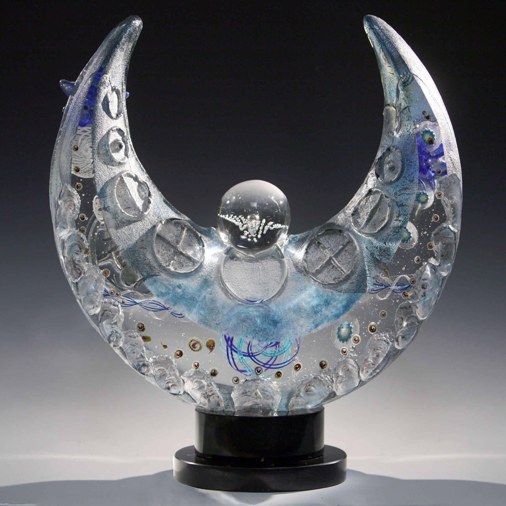A clear glass sculpture of a crescent moon on a black base