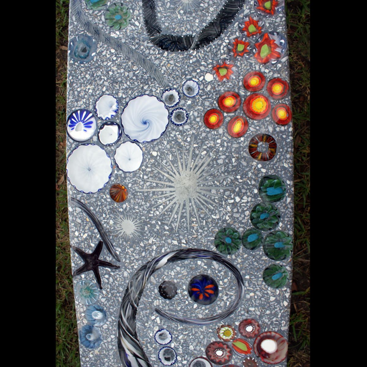 A mosaic of seashells and flowers is sitting on the grass.