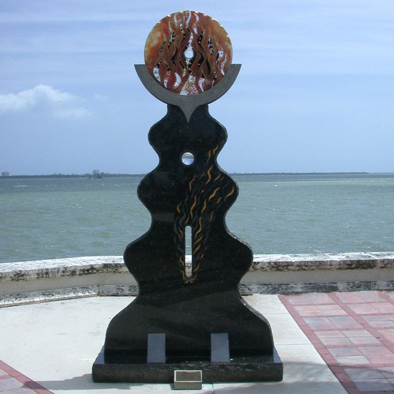 A statue with a hole in the middle of it stands in front of a body of water